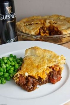 a piece of pie on a plate with peas and a bottle of guinness next to it