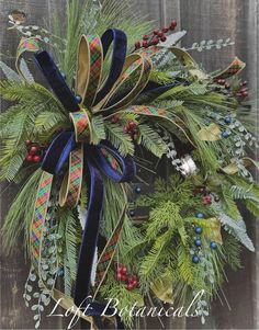 a christmas wreath on a wooden fence with blue ribbon and holly berries, pine cones and evergreens