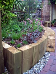 a garden with flowers and plants growing in the ground next to a wooden fence on a brick walkway