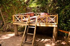 a wooden bench sitting in the middle of a forest next to a ladder with blankets on it