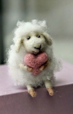 a stuffed sheep with a pink heart in its mouth sitting on top of a purple box