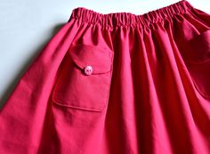 a pink skirt with a button on the front and pocket at the back, sitting on a white surface