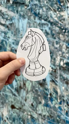 a hand holding up a sticker with a horse on it's face in front of an abstract background