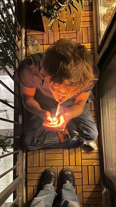 a man sitting on the floor holding a lit candle in his hand and looking down at it