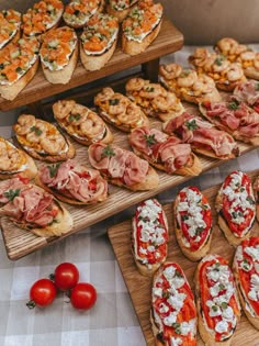 many different types of appetizers on wooden trays next to tomatoes and bread