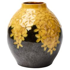 a yellow and black vase with flowers on it's sides, sitting in front of a white background