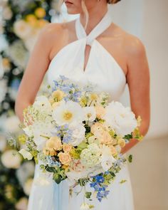 a woman in a white dress holding a bouquet of flowers and wearing a blue ribbon around her neck