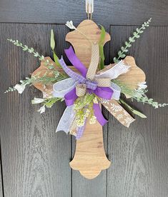 a cross made out of wood with purple ribbon and flowers hanging on the front door