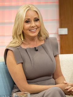 a woman sitting on top of a couch in front of a tv screen wearing a gray dress