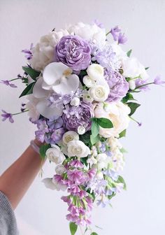 a bride's bouquet with purple and white flowers on the bottom is held by her hand