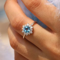 a woman's hand holding a ring with an oval blue topazte surrounded by small white diamonds