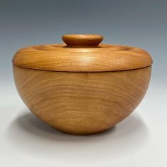 a wooden bowl with a lid on a white tableclothed surface and grey background