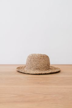 Front view of Handwoven Hat on an Oak Dining Table Against a White Wall. - Saffron and Poe Lightweight Packable Sun Hat For Beach, Lightweight Packable Bucket Hat For Beach, Lightweight Packable Sun Hat For The Beach, Casual Natural Straw Hat Packable, Casual Natural Color Packable Straw Hat, Natural Toquilla Straw Bucket Hat With Flat Brim, Lightweight Toquilla Straw Bucket Hat With Short Brim, Lightweight Flat Brim Hat For Beach, Lightweight Flat Brim Hat For The Beach