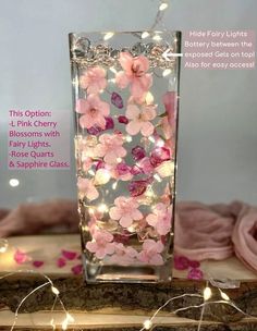 a glass vase filled with pink flowers and fairy lights