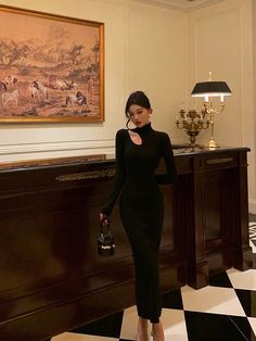 a woman in a black dress standing next to a table with a lamp on it