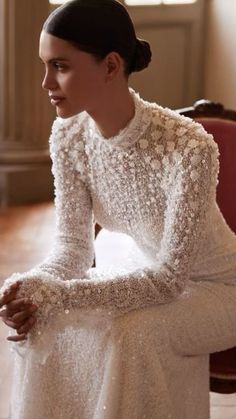 a woman sitting on top of a wooden floor wearing a long sleeved white dress