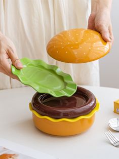 a person holding a green leaf over a plastic container filled with chocolate sauce on top of a white table