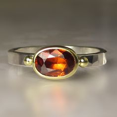 Gorgeous, natural faceted spessartite(orange garnet) garnet set in solid 18k bezel on hammered(flattish hammer) sterling silver band(approx. 2.5mm wide x 1.5mm thick). An 18k gold ball has been soldered to the band on each side of the spessartite garnet. The spessartite  has a backsheet of polished fine silver(closed setting). The spessartite garnet measures 5.6 X 7.9mm and weighs 1.35cts. All metal is from recycled sources. This ring is a size 7 and I cannot resize. Attractively boxed. Photos h Spessartite Garnet, Unusual Rings, Garnet Gem, Hammered Sterling Silver, Garnet Ring, Garnet Rings, Sterling Silver Bands, Fine Silver, Silver Band