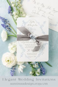 the wedding stationery is laid out on top of blue and white flowers with silver ribbon