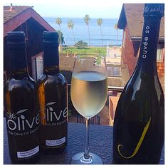 three bottles and two glasses of wine on a table with the ocean in the background