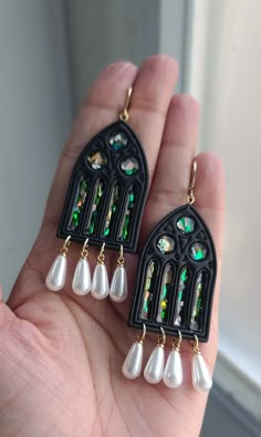 a pair of black earrings with white pearls and green glass bead details on them