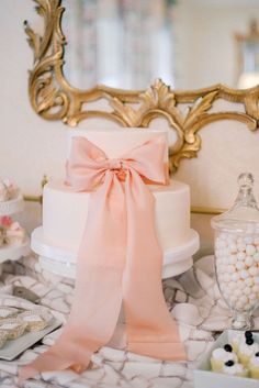 there is a wedding cake with pink ribbon on the table next to other desserts