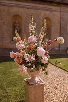 a vase filled with lots of flowers sitting on top of a stone block in front of a building