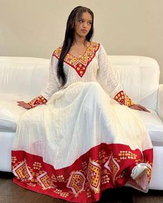 Ethiopian and Eritrean traditional white dress with intricate red, yellow, and gold embroidery. The dress has a distinctive cultural style, possibly Ethiopian or Eritrean, based on the patterns and colors. elegant dress looks like beautiful dress any ceremony Habesha Traditional Dresses, White Traditional Wear With Zari Work Maxi Length, White Traditional Maxi With Zari Work, White Bollywood Kaftan With Traditional Drape, White Kaftan With Resham Embroidery For Navratri, Ceremonial White Dabka Dresses, Festive White Kaftan For Transitional Season, Transitional Festive White Kaftan, Bollywood White Kaftan With Zari Work