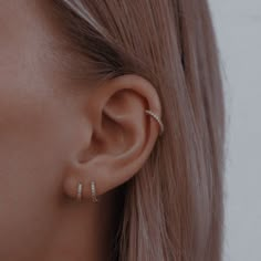 a close up view of a woman's ear with three small diamond hoops