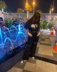 a woman standing in front of a fountain with blue lights on it's sides