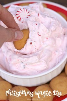 a hand dipping a cookie into a bowl of candy canes on top of cookies