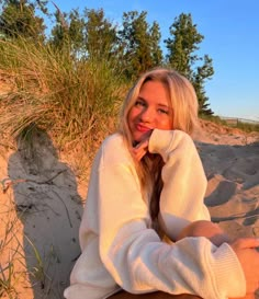 a woman sitting in the sand with her hand on her chin and looking at the camera