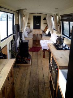 the inside of a small camper with wood floors and white drapes on the windows