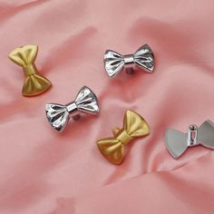 four different colored bows are on a pink cloth with silver and gold pins in the shape of bow