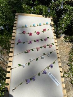 several necklaces with flowers on them sitting on a wooden board in front of some bushes