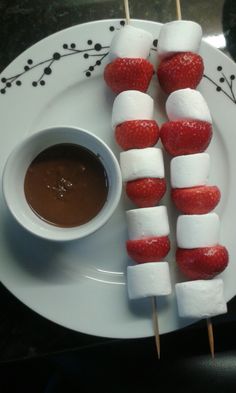 strawberries and marshmallows are arranged on skewers with chocolate sauce