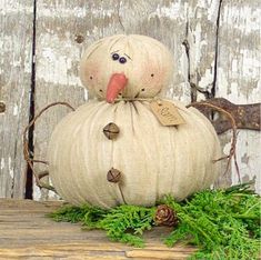 a white pumpkin sitting on top of a wooden table next to some green leaves and pine cones