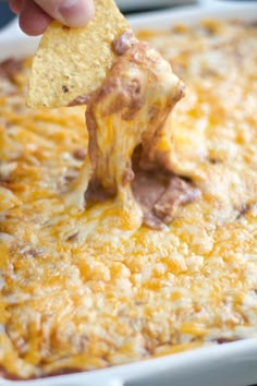 a hand dipping a tortilla chip into a casserole dish with cheese