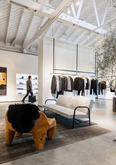 a man is walking past a bench in a clothing store with clothes hanging on racks