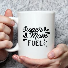 a woman holding a white coffee mug with the words super mom fuel on it