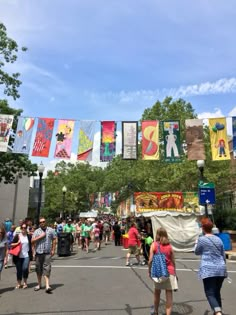 many people are walking down the street in front of banners hanging from trees and buildings