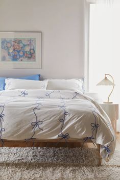 a bed with white sheets and blue bows on it in a bedroom next to a window