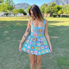 a woman standing in the grass wearing a dress with crocheted squares on it