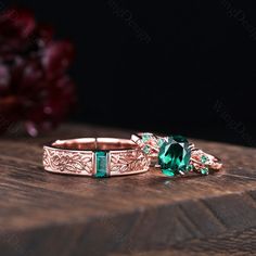 two wedding rings with green stones on top of each other, sitting on a wooden table