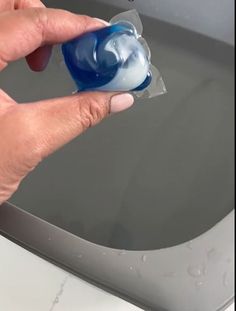 a hand holding a blue and white object in front of a toilet