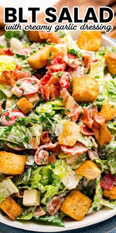 a salad with croutons and bacon on top in a white bowl next to some bread cubes