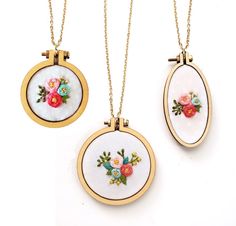 two necklaces with flowers on them are hanging from gold colored chains and one has a white background