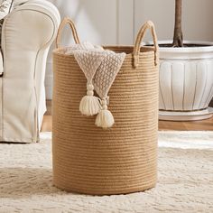 a large round basket with tassels on the handles and handle is shown in front of a white couch