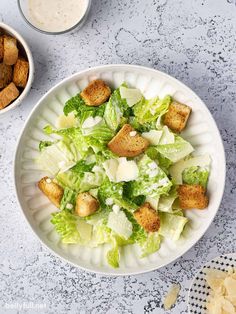 a white bowl filled with lettuce and croutons next to a cup of ranch dressing