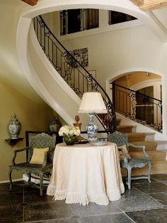 a table with a lamp on it in front of a stair case and some chairs